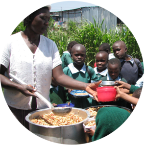 Afrikanische Schulkinder drängeln sich um die Essensausgabe. Eine Frau mit einem großen Topf Bohnen verteilt das Essen.