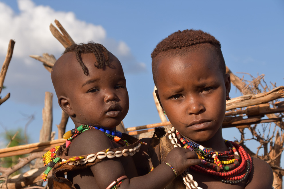 Portrait eines afrikanischen jungen Mädchens. Das Mädchen ist selbst noch ein Kind, trägt aber bereits ihr eigenes Kind auf dem Arm. Beide blicken traurig und verloren in die Kamera.