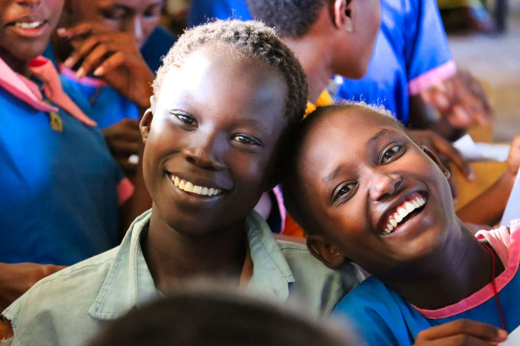 Zwei Jugendliche, etwa 10-12 Jahre alt, ein Mädchen und eine Junge, die fröhlich in die Kamera lachen. Im Hintergrund die Klassenkameraden.