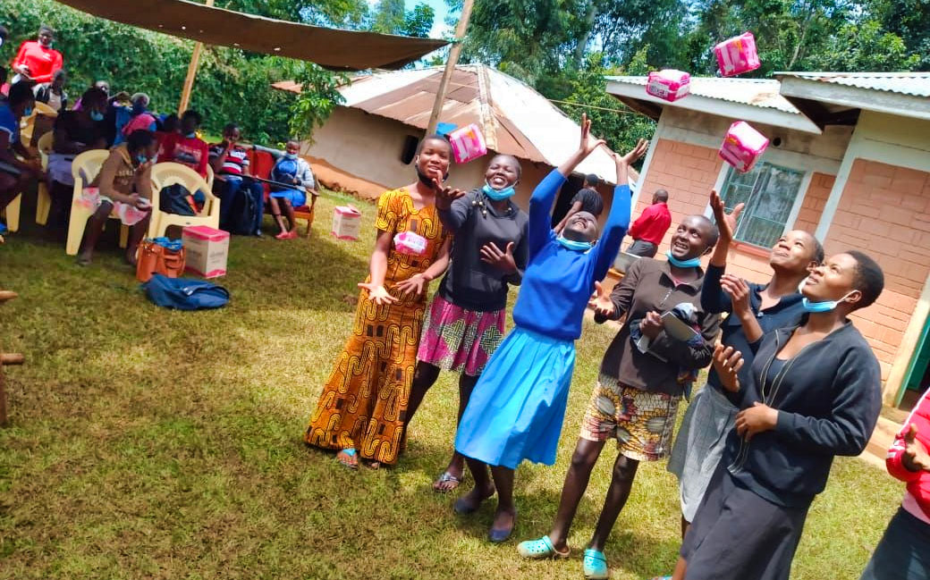 Junge Mädchen aus Kenia haben Menstruationsartikel geschenkt bekommen. Sie werfen sie glücklich in die Luft.