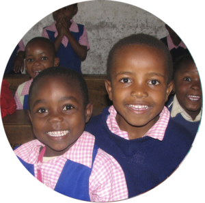 Zwei Schulkinder aus Kenia strahlen fröhlich in die Kamera. Mäden und Junge sind etwa 6 Jahre alt.