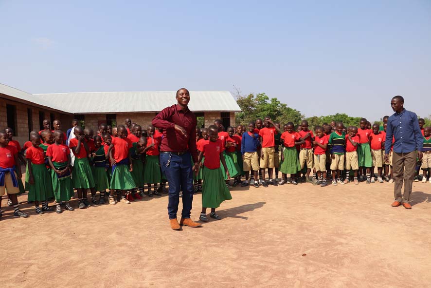 Eine Schulklasse in Tansania steht mit ihrem Lehrer vor dem Schulgebäude und freuen sich über ihre neue Schule.