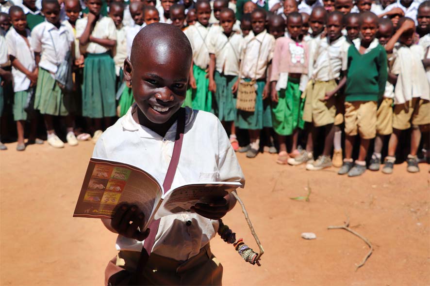 Ein junge in Afrika strahlt über sein eigenes Schulbuch. Die anderen Schüler warten noch, bis sie an der Reihe sind.