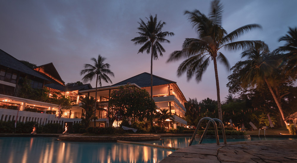 Abendstimmung mit Palmen. Eine schöne Hotelanlage. Im Vordergrund ein Swimmingpool.