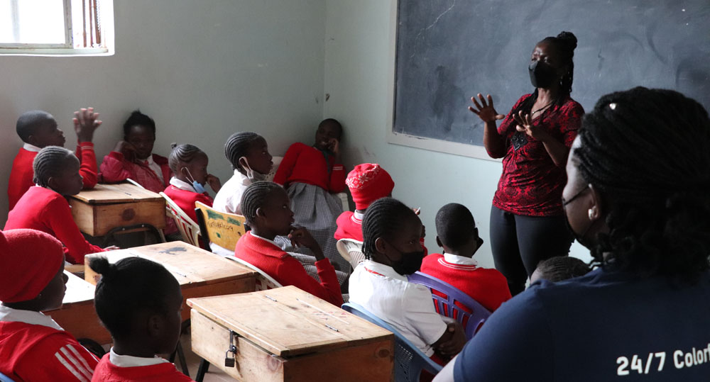 Eine Lehrerin steht vor einer Klasse und unterrichtet eine Gruppe afrikanischer Kinder in roter Schuluniform