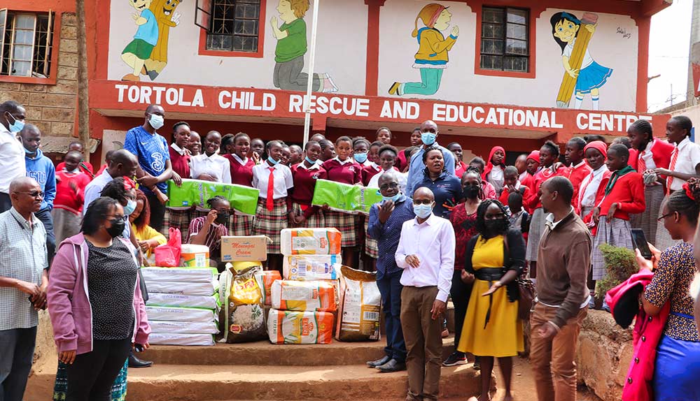 Eine Gruppe von Menschen, Lehrern und Schülern stehen vor der Schule in Tortola Nairobi. Sie haben kostenlose Hygieneartikel für die Mädchen aufgestapelt.