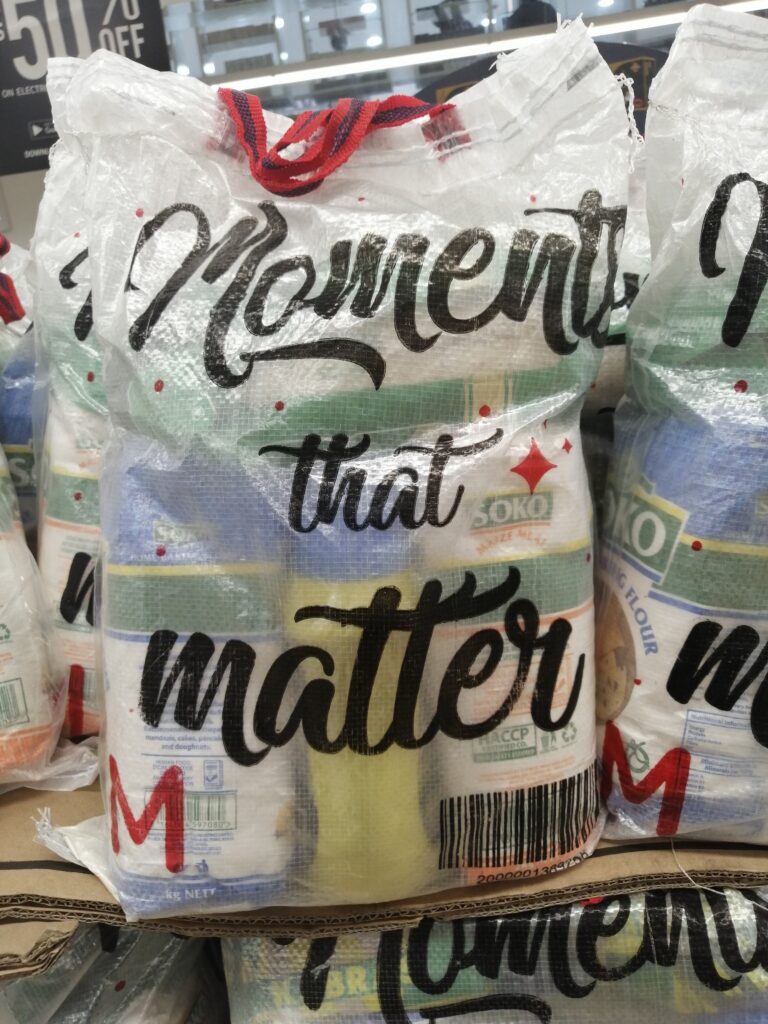 Gestapelte Säcke mit Maismehl in einem kenianischen Supermarkt, bedruckt mit dem Schriftzug „Moments that matter“.