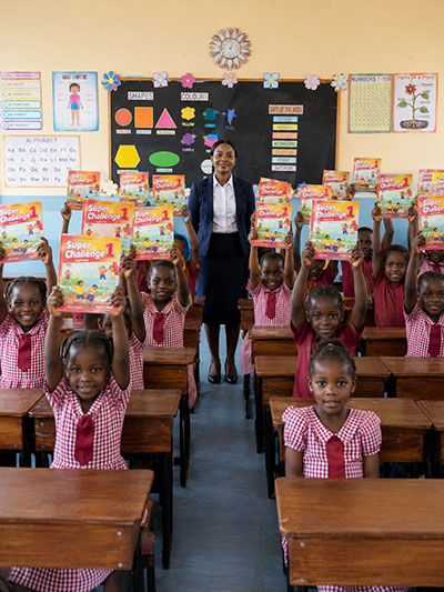 Lehrerin hält einen Atlas vor ihrer Schulklasse in Kenia – Bildung in Ostafrika zwischen Anspruch und Realität