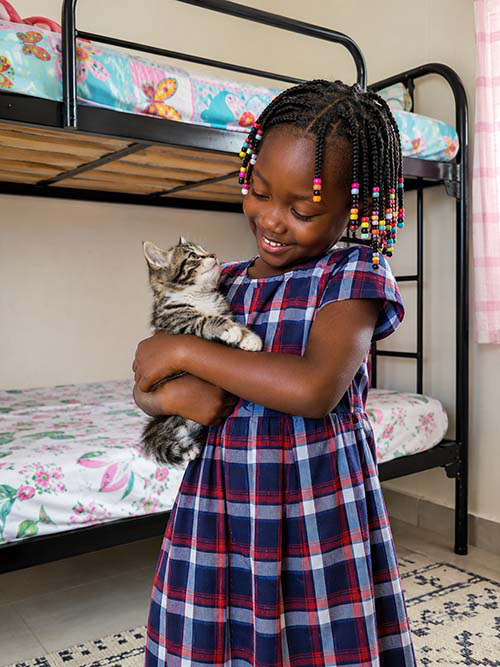 L&auml;chelndes M&auml;dchen in Afrika h&auml;lt eine junge Katze auf dem Arm.